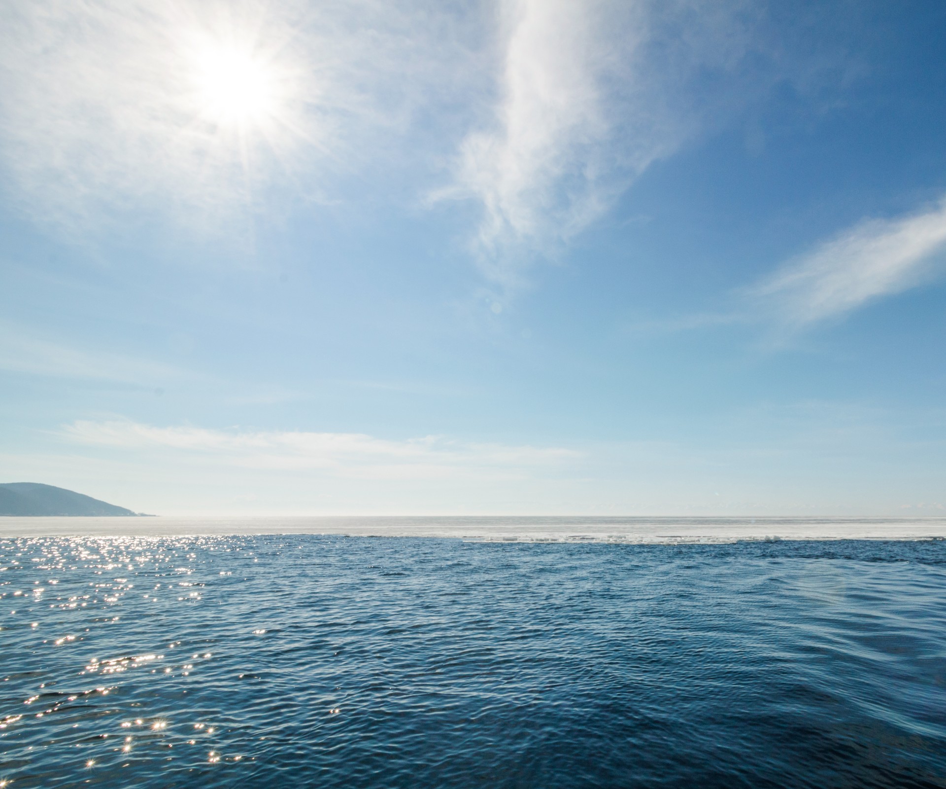 Wide angle view of the sea with sun reflections and blue sky with light veil clouds