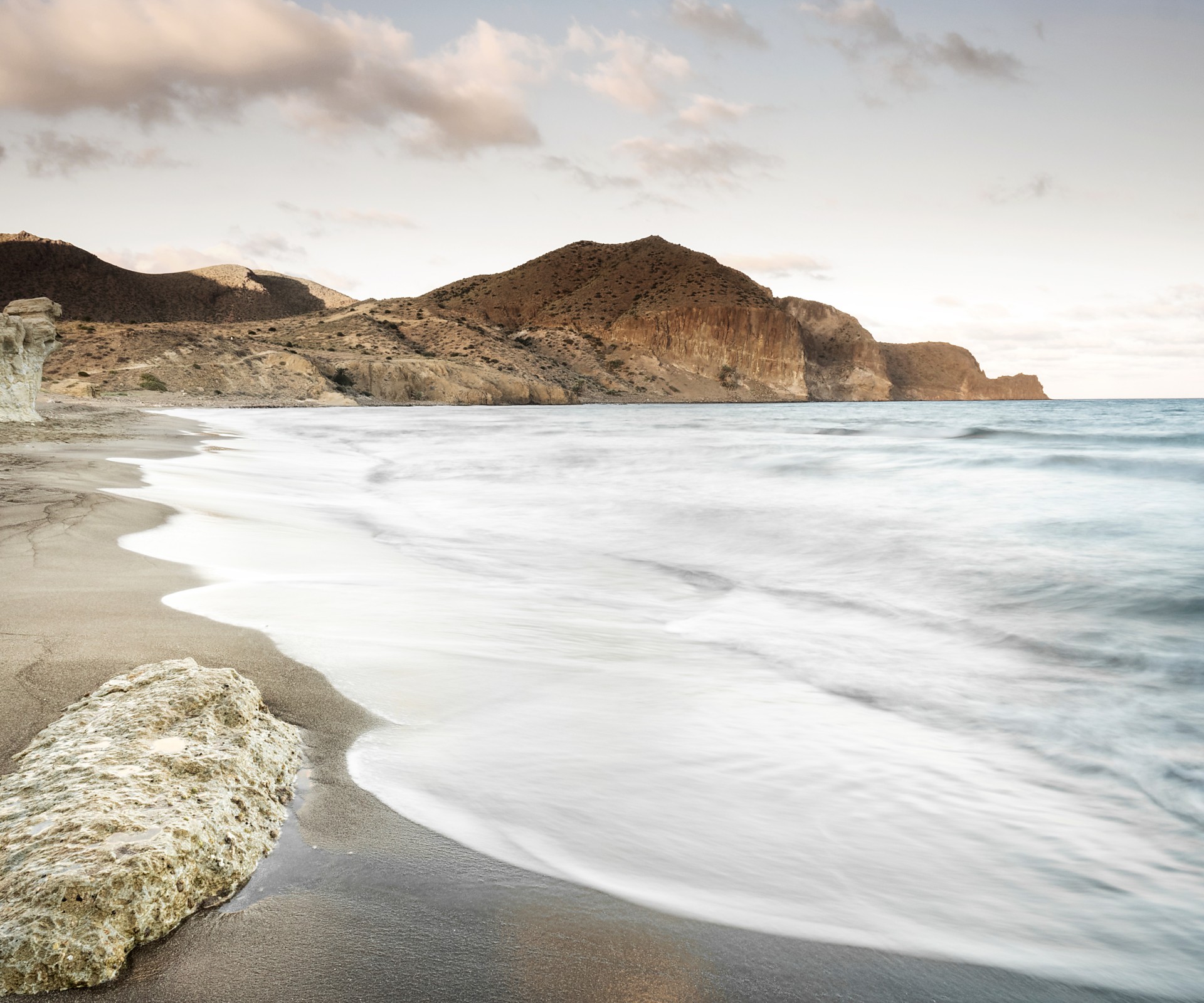 Playa con arena oscura y acantilados en el fondo durante el atardecer    	