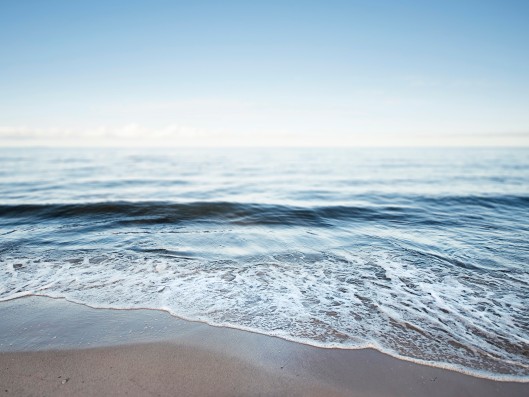 lightly foaming waves gently crashing on a sandy beach under a blue sky    	