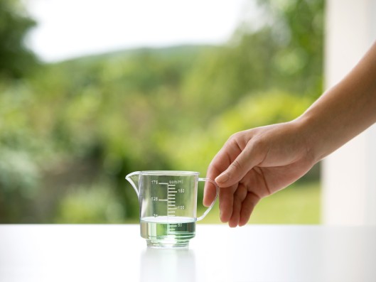 One hand reaches for a small measuring cup filled with Frosch sensitive detergent aloe vera	